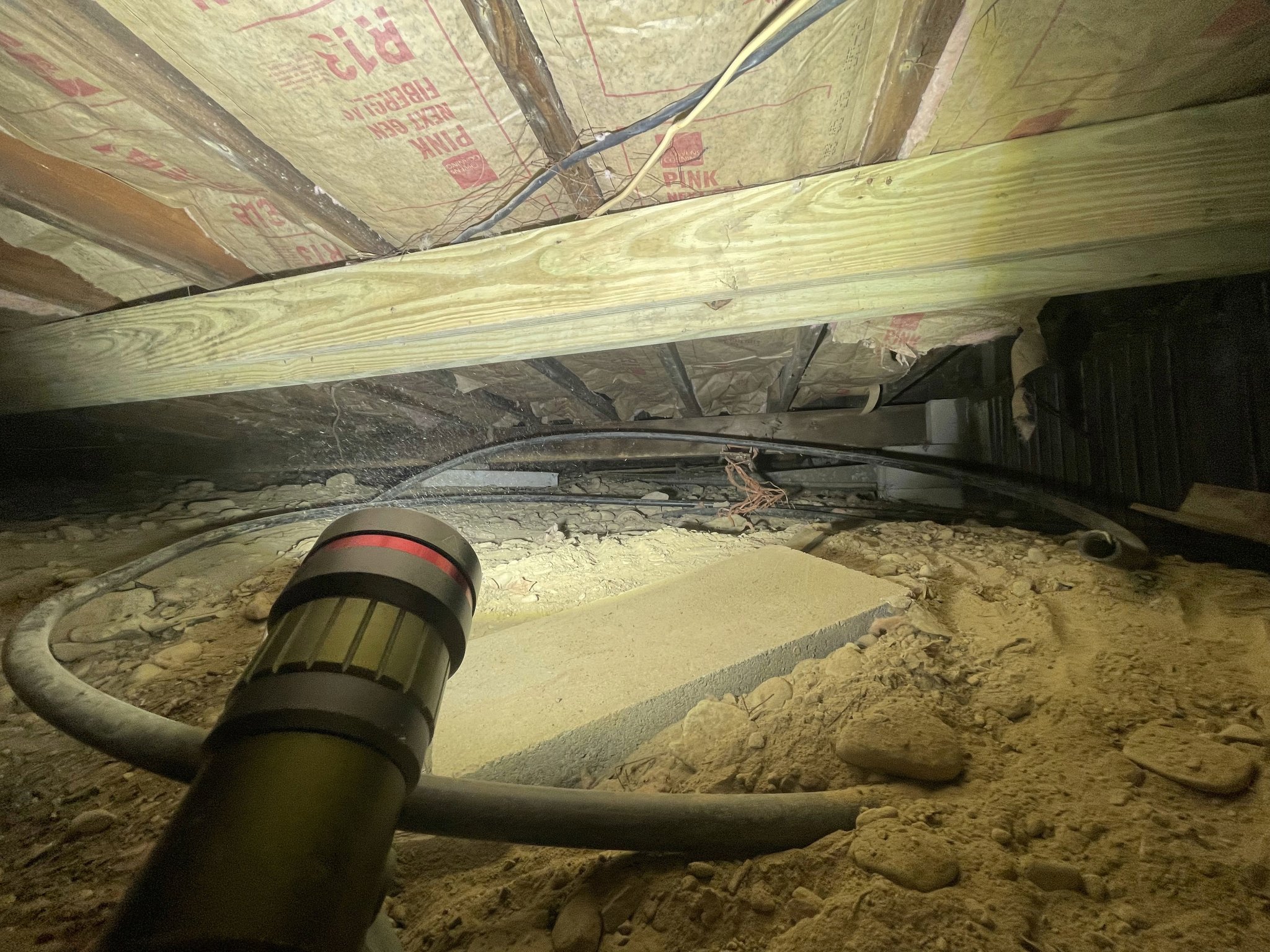 Vacuum extraction hose on cleared soil floor — insulation fully removed, joists exposed and documented, crawlspace staged for vapor barrier installation